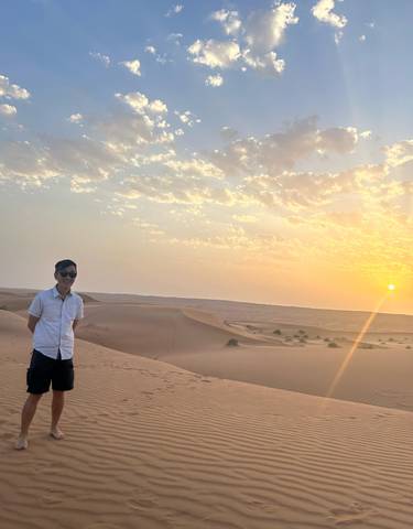 A person standing in a desert during sunset with clear skies and sand dunes.