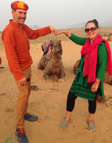 Two people with a camel on sandy terrain.