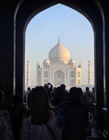 Taj Mahal viewed through an archway, crowded with tourists.