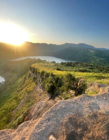 Landscape view of a hilly terrain with a lake and sun rays breaking through, creating a picturesque scene.