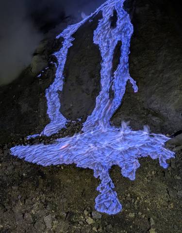 Nighttime photo of blue flames on rocky ground, likely at Ijen Volcano.