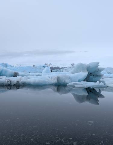 Icebergs floating on calm water under a cloudy sky.