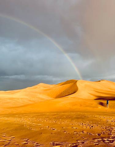 Sand dunes in the desert with a rainbow and stormy sky.