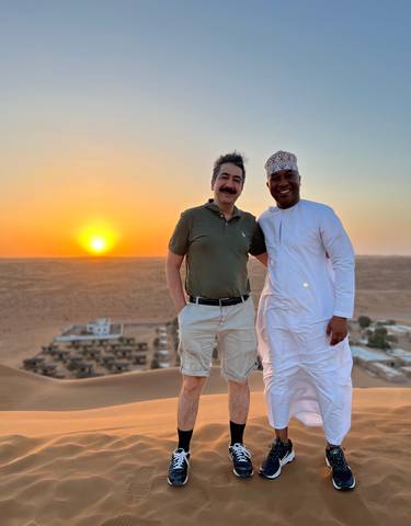 Two people posing with a sunset over desert landscapes.
