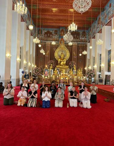 Group of people in a temple in front of a golden Buddha statue