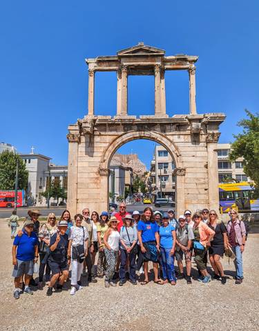 Large group of people posing under an ancient arch with the Acropolis in the background.