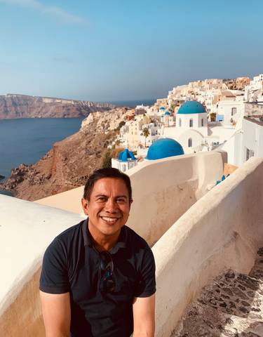 Person smiling with Santorini's iconic blue-domed buildings.