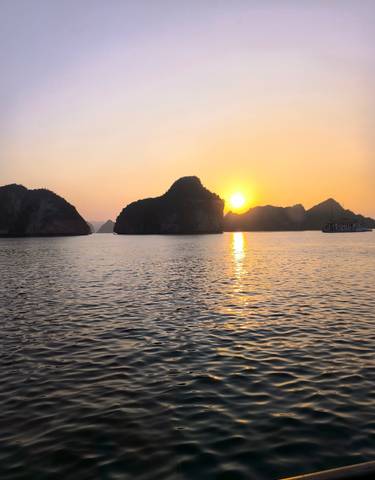 Sunset over Halong Bay with traditional boat on the water.