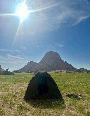 A tent with a backdrop of a towering rock formation under a clear blue sky.