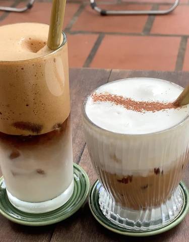 Two glasses of Vietnamese iced coffee with frothy tops.
