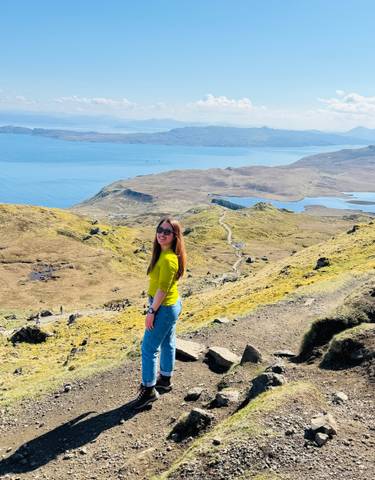 Woman smiling on a cliffside overlooking a coastal landscape.
