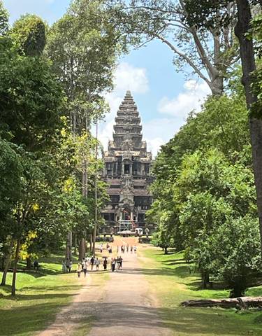 A view of the Angkor Wat temple through a lush green walkway.
