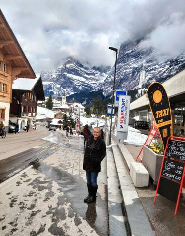 Person posing in a snowy mountain village with shops and signs.