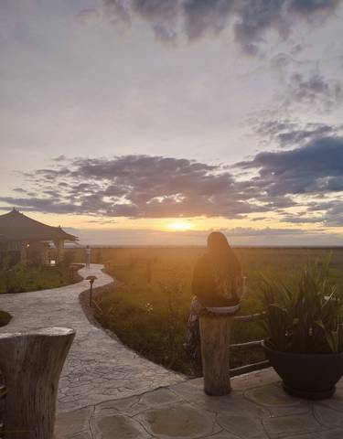 Individuals watching a sunset over savannah landscape.