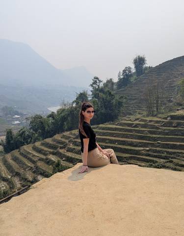 A woman sitting on a rock in front of terraced fields.