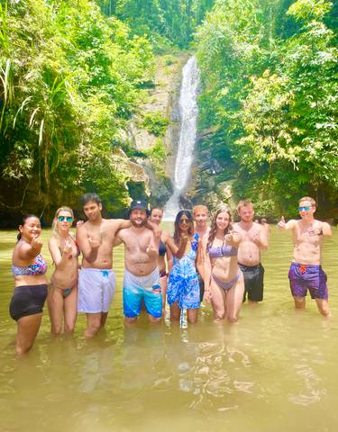 Group of friends posing in front of a waterfall in a tropical setting.