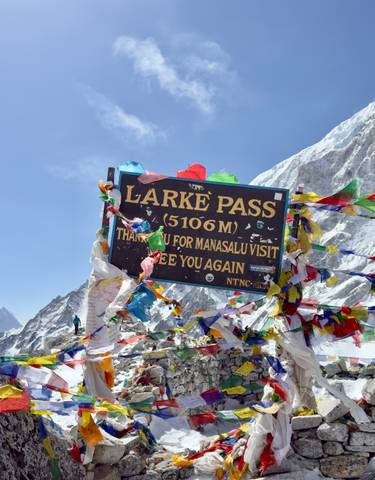Sign at Larke Pass with colorful flags against mountain backdrop.