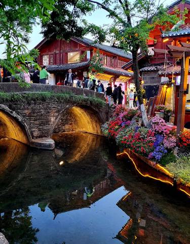 Scenic view of a traditional bridge over a stream with flowers and people.