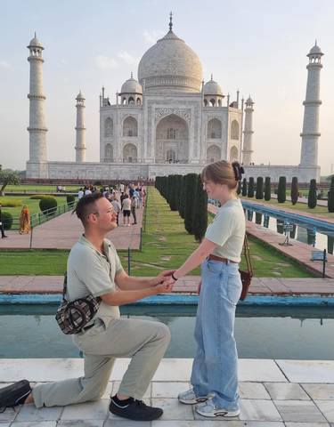 A couple in front of the Taj Mahal, with the man on one knee proposing.