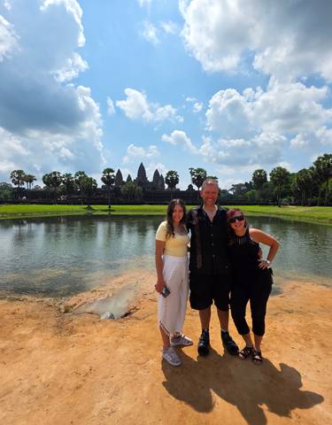Smiling group posing with Angkor Wat temple in background.