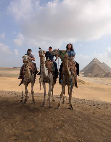 Group of people riding camels in front of pyramids.