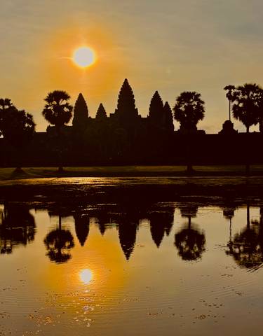 Silhouette of Angkor Wat with reflection on the water during sunset.