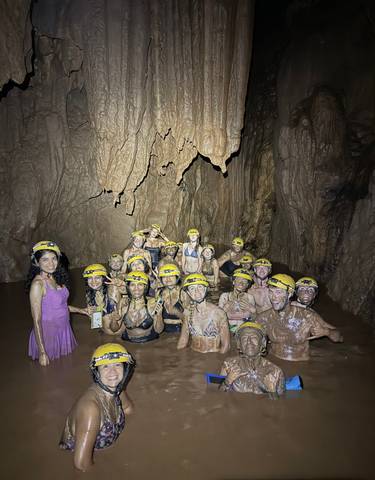 Group caving adventure with people covered in mud and wearing helmets.