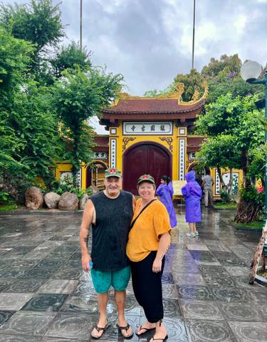 Couple posing in front of an ornate temple structure with others around.