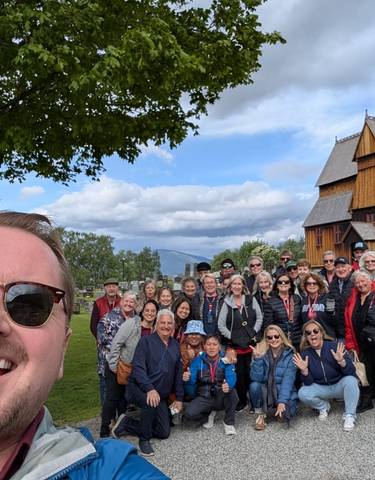 A group of tourists posing in front of a wooden church.