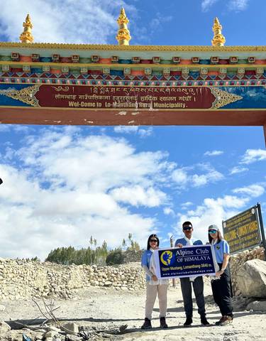 Three people standing under a decorated archway with a sign for Lo-Manthang.