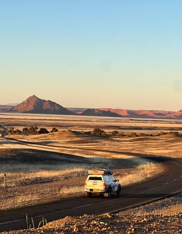 Car on a winding road with red desert hills in the background.