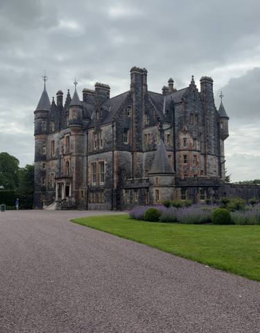 Large historic stone castle with gardens and a cloudy sky.