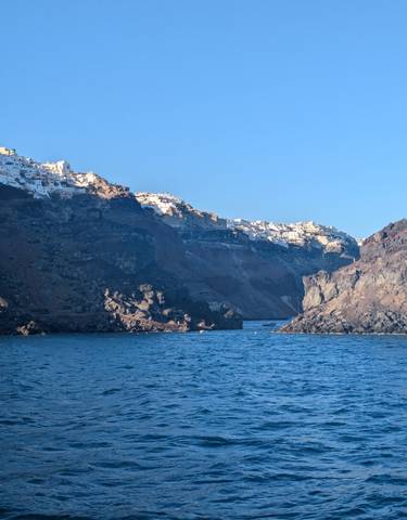 Coastal village with white buildings on a rocky cliff by the sea, likely Santorini, Greece.