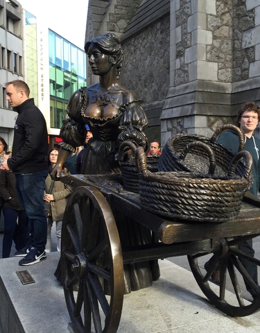 Statue of a woman with baskets observed by tourists.