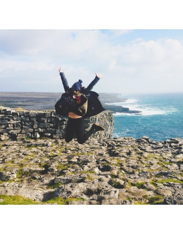 Person jumping in the air on a rocky coastline.