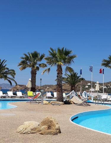 Beach resort with palm trees and sun loungers by a pool.