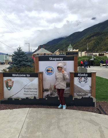 Person beside Alaska signage with mountains in the background.