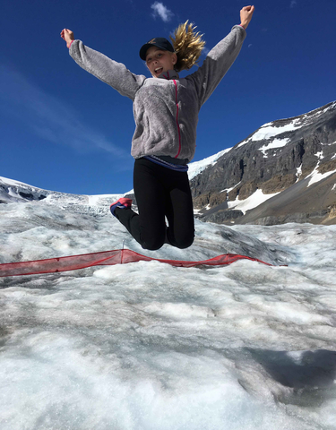 Person jumping on a glacier with clear skies and mountains.