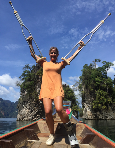 Woman smiling while holding crutches with limestone cliffs in the background.
