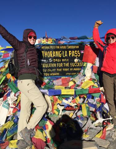 Two people celebrating at Thorong La Pass with prayer flags.