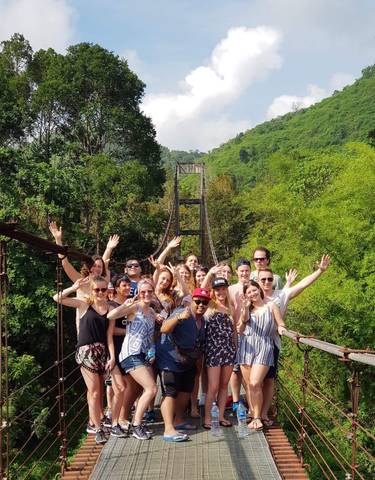 Group posing in front of a suspension bridge and lush green trees.