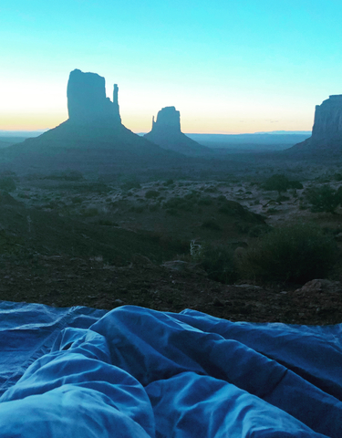 A sleeping bag set up among rock formations during sunrise.