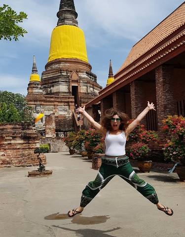 Woman joyfully posing in front of a historic temple with vibrant flowers.