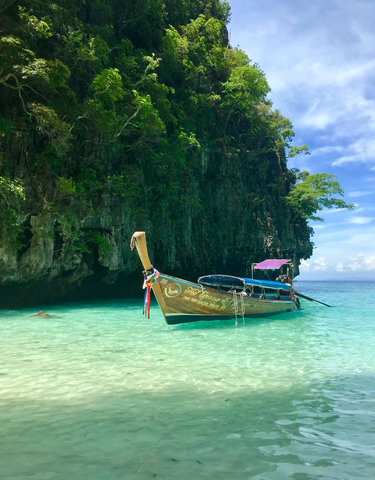 A traditional long-tail boat in clear turquoise waters with lush green cliffs in the background.