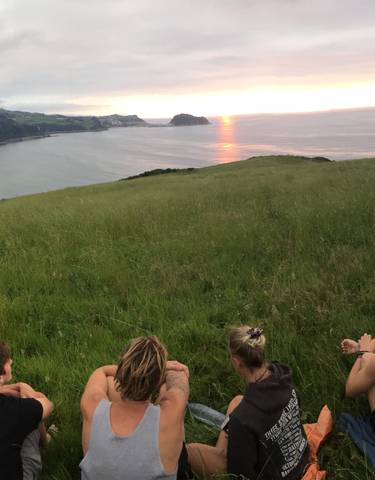 People sitting on a hill enjoying a sunset view over the ocean.