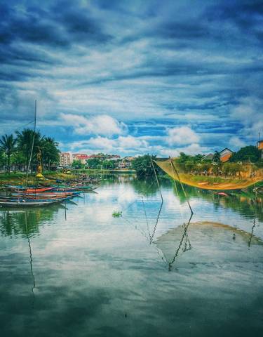 Boats on a river, with fishing nets and buildings in the background.