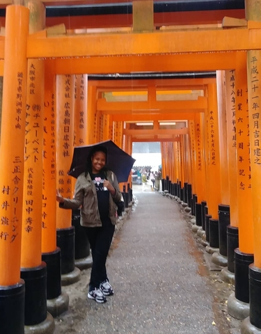 Person with an umbrella walking through a series of torii gates.