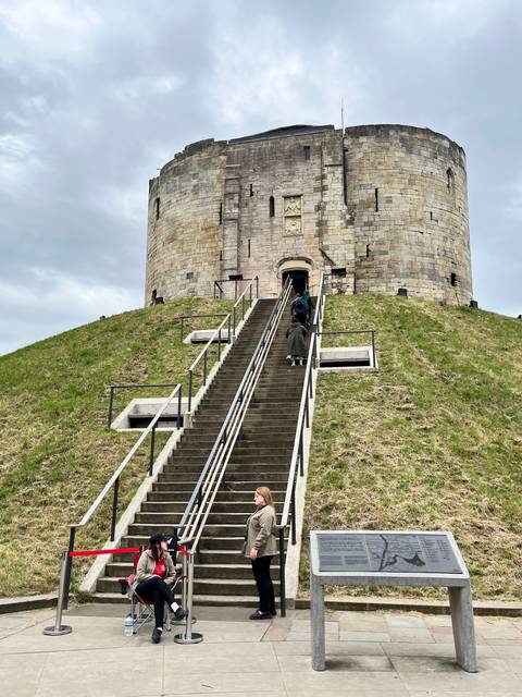       Castle ruin on a hill with tourists ascending stairs.
  