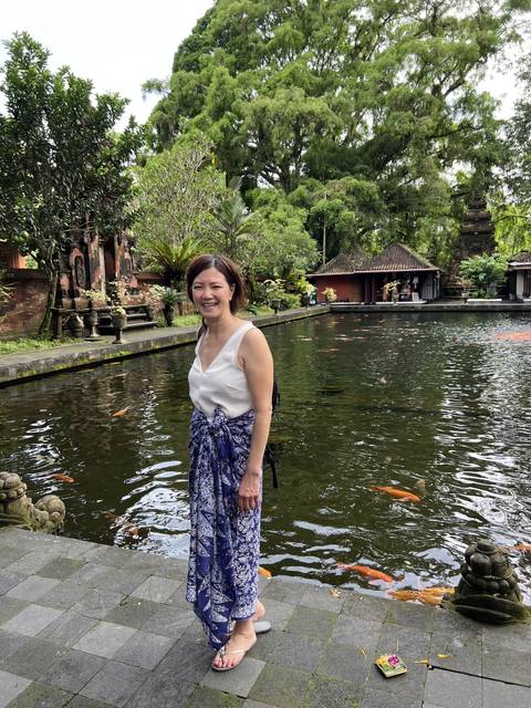       Person standing by a pond with colorful fish, traditional buildings in the background.
  