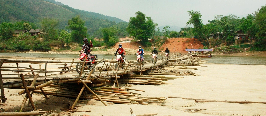 Riders crossing a bamboo bridge in a rural area.